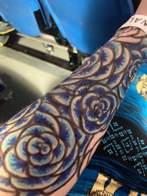 A forearm, with tattoo-marker art of many blue flowers.
