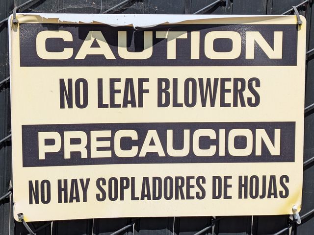 a sign on a cyclone fence:

CAUTION
NO LEAF BLOWERS

PRECAUCION
NO HAY SOPLADORES DE HOJAS