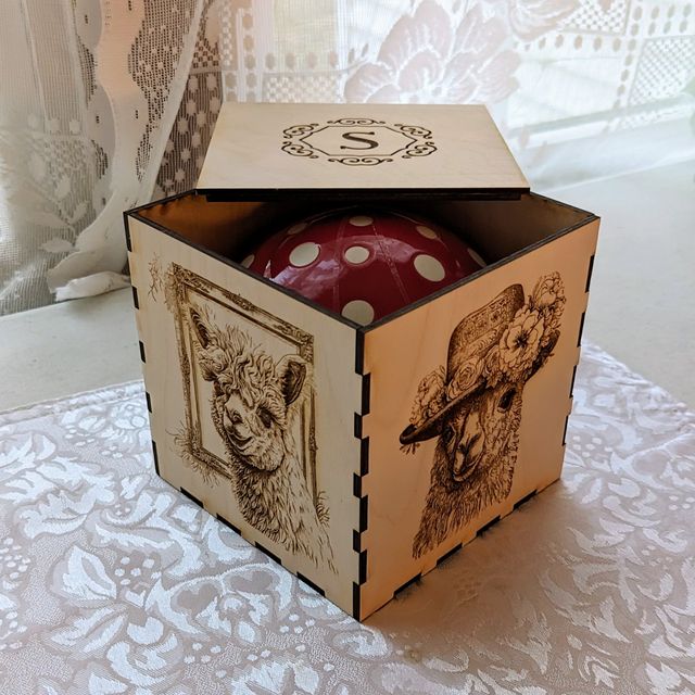 Laser cut box with engraved alpacas and a hint of a mushroom mug inside.