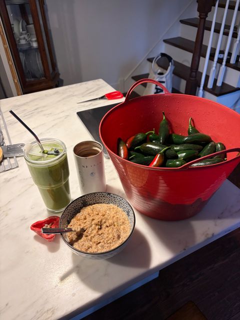 A basket of jalapeño peppers alongside a bowl of oatmeal and beverages. The basket is huge.